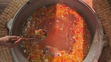 Chef mixes meat soup with vegetables in a large cauldron with a slotted spoon video