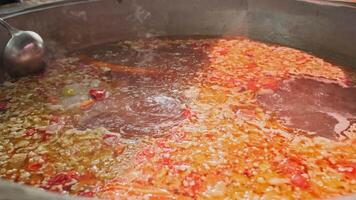 Chef mixes meat soup with vegetables in a large cauldron with a slotted spoon video