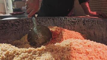 el cocinero lanzamientos arroz con un ranurado cuchara en un grande caldera mientras Cocinando pilaf video