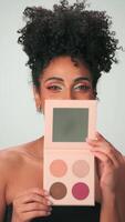 un joven mujer con brillante maquillaje se ríe y se regocija, participación un conjunto de productos cosméticos en su mano video