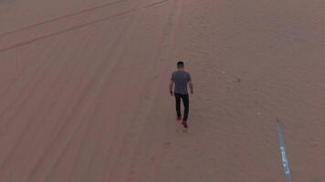 un hombre caminando a lo largo un cubierto de arena asfalto la carretera video
