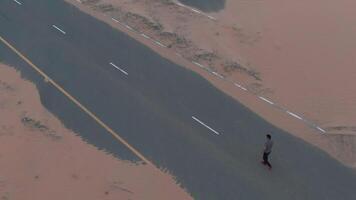 un' uomo a piedi lungo un' coperto di sabbia asfalto strada video