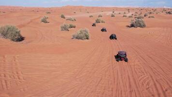 A drone flies over a caravan of buggies driving through the desert sand video