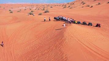 A drone flies over a caravan of buggies standing on a desert sand dune. video