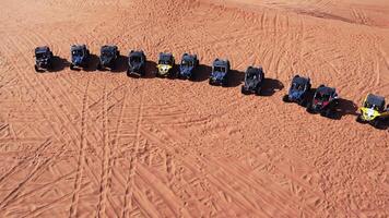 A drone flies over a caravan of buggies standing on a desert sand dune. video