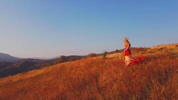 Drone flies over young woman in autumn outfit on meadow in mountains on sunset background video