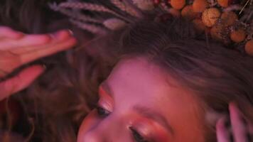 Close-up shot of the face of a young woman in an autumn outfit of branches, leaves and ears of corn, flying in the grass among scattered apples. video