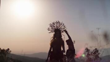 Tashkent, Uzbekistan - 1 9 2020. Film crew with a young female model in an autumn designer dress made of flowers and a headdress made of spikelets on the background of the sunset in the mountains. video