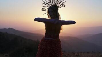Young female model in designer headdress made of spikelets and dress made of flowers and grass on the background of sunset in the mountains. video