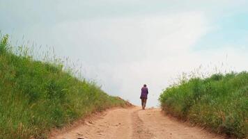 antiguo hombre en un casquete camina lejos desde el cámara abajo el país la carretera video