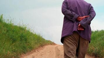 antiguo hombre en un casquete camina lejos desde el cámara abajo el país la carretera video