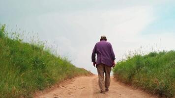 Old man in a skullcap walks away from the camera down the country road video