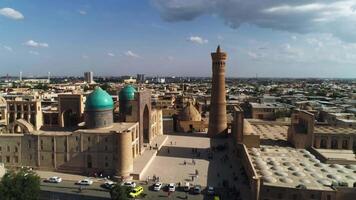 ein Drohne fliegt Über ein Gruppe von Touristen im Vorderseite von das Tore von das architektonisch Komplex poi-kalon im alt Buchara, Usbekistan. wolkig wolkig Tag. video