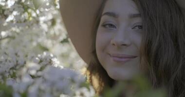 fechar-se do menina vestindo uma chapéu e cheirando a floração ramo do maçã árvore video