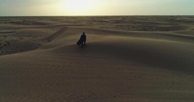 en Drönare flugor över en man i arab kläder gående på de sand sanddyner av de öken- på de bakgrund av de solnedgång video