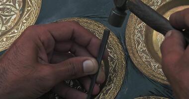 A master embosser creates a pattern on a copper plate using ancient technologies. video