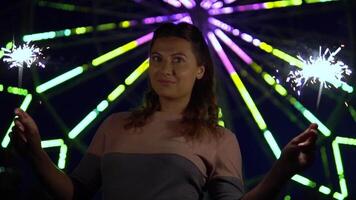 Beautiful happy girl holding fireworks in hands on a background of multi-colored lights having a good mood. slow motion video