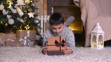 familie kerstmis, pret partij, blijven Bij huis, nieuw jaar viering. jongen opent een geschenk doos Bij huis in de buurt de Kerstmis boom video