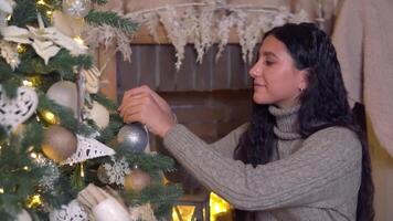 família Natal, Diversão festa, fique às lar, Novo ano celebração. uma mulher decora uma Natal árvore de suspensão uma colorida bola video
