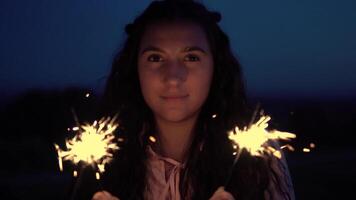 bellissimo giovane ragazza con lungo capelli con fuochi d'artificio nel mani su un' sfondo di un' notte città. lento movimento. video