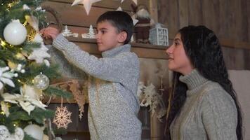 familie kerstmis, pret partij, blijven Bij huis, nieuw jaar viering. mam en zoon versieren de Kerstmis boom met mooi ballen en knuffel video