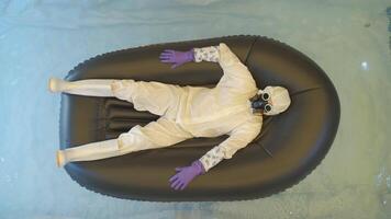 Man in chemical protection suite is lying in an boat drifting on the water. video