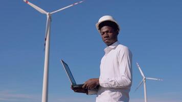 African American electrician engineer standing on the background of a windmill at an air power plant with a tablet in his hands video