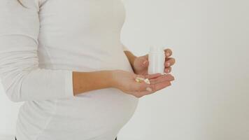 Pregnant woman stands on a white background and pours pills on the palm video