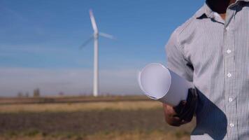 African American electrician engineer standing on the background of a windmill at an air power plant with a drawing in his hand. Close-up view of hand and scroll video