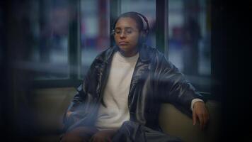 A woman sitting on a couch wearing headphones in front of a window at midnight video