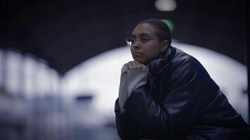 ein Frau im ein schwarz Jacke ist Sitzung im ein dunkel Zimmer mit ihr Hände auf ihr Kinn video