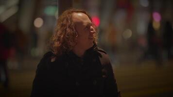 une homme avec longue frisé cheveux est vu séance sur le trottoir à nuit, contemplant vie. le obscurité de le réglage ajoute une sens de mystère et introspection à le scène video