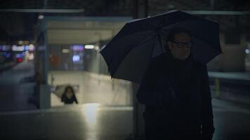 homme détient parapluie dans le pluvieux obscurité, blindage de le humide asphalte video