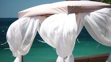 bungalows hav. strand vardagsrum säng med vit silkig gardiner. vardagsrum säng med tak på havet. strand stolar och solskydd. sommar semester tillflykt begrepp. video