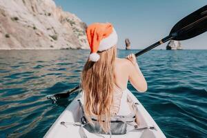 Woman in kayak back view. Happy young woman in Santa hat floating in kayak on calm sea. Summer holiday vacation and cheerful female people relaxing having fun on the boat. photo