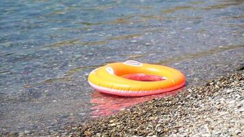 stänga upp sudd uppblåsbar simma ringa av en orange munk flytande på de lugna hav. sommar tema, ingen. uppblåsbar ringa på strand, orange simning ringa cirkel flyter simma ringa slå samman flyta vatten leksaker video