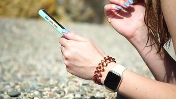 Woman with smartphone. Close-up of woman's hands holding vertical mobile phone and swiping up finger application page against background of sea and beach video