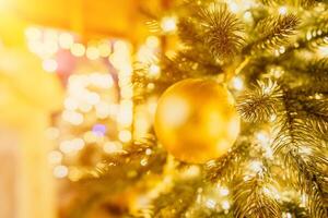 A Christmas tree with gold ornaments and lights. The tree is decorated with gold balls and is lit up with lights. The tree is placed in a room with a window photo