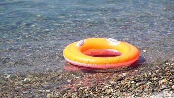 dichtbij omhoog rubber opblaasbaar zwemmen ring van een oranje donut drijvend Aan de kalmte zee. zomer thema, niemand. opblaasbaar ring Aan strand, oranje zwemmen ring cirkel drijft zwemmen ring zwembad vlotter water speelgoed video