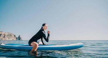 Woman sup yoga. Happy sporty woman practising yoga pilates on paddle sup surfboard. Female stretching doing workout on sea water. Modern individual female hipster outdoor summer sport activity. photo