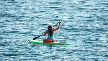 mare donna sup. silhouette di contento positivo giovane donna nel blu bikini, fare surf su verde cenare tavola attraverso calma acqua superficie. idilliaco tramonto. attivo stile di vita a mare o fiume. lento movimento video