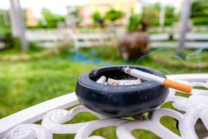 Cigarette burning with smoke on ceramic ashtray photo