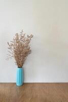 Dried flower in turquoise vase on wooden table over beige wall photo