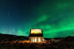 Aurora borealis, Northern lights glowing over luxury hotel on volcanic wilderness in winter at Iceland photo