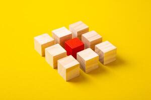 Red wooden block standing out from the group wooden blocks on yellow background. Leadership and divergent views concepts photo