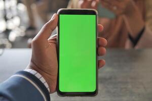 mano de hombre joven usando un teléfono inteligente con pantalla verde en el café foto