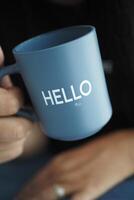 women holding a blue coffee cup with hello word photo