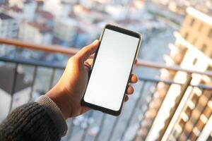 mano de hombre joven usando un teléfono inteligente con pantalla verde contra edificios de la ciudad foto