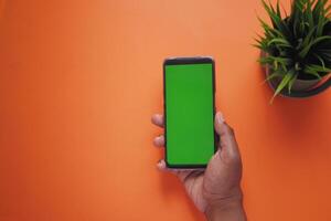 top view of young man hand using smart phone with green screen on orange color background photo