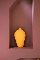 A wooden artifact, a yellow vase, sits in a niche on a purple wall photo